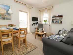 A living room with a sofa, a dining table with chairs, a television, and a bookshelf. - 14B Canal Wharf, Ripon (Ripon)