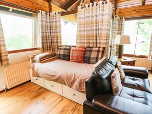 A cozy room with a bed, a leather sofa, and a window with curtains. - Katchana: A Tranquil Retreat in Kincraig (Kingussie)