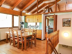 A wooden dining table with chairs, a kitchen with yellow cabinets, and a staircase with a railing. - Katchana: A Tranquil Retreat in Kincraig (Kingussie)