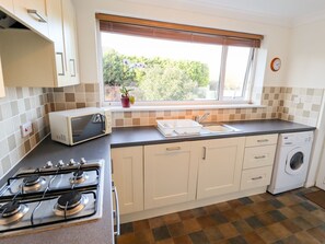 A compact kitchen with a gas stove, microwave, sink, and washing machine. - Acre View, Sutton-On-Sea (Mablethorpe)