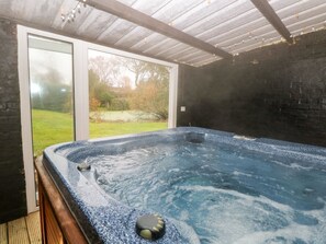 Ein Whirlpool mit einer Holzdielen-Terrasse, einer Glastür, die nach draußen führt, und einer Backsteinwand.