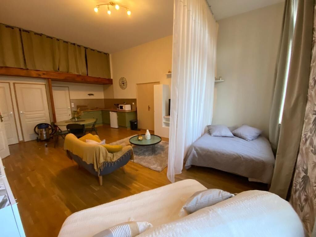 A room with a bed, a sofa, a small table, and a kitchen area.