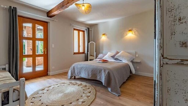 Un dormitorio con cama, piso de madera, alfombra redonda, puerta con ventana y viga en el techo.