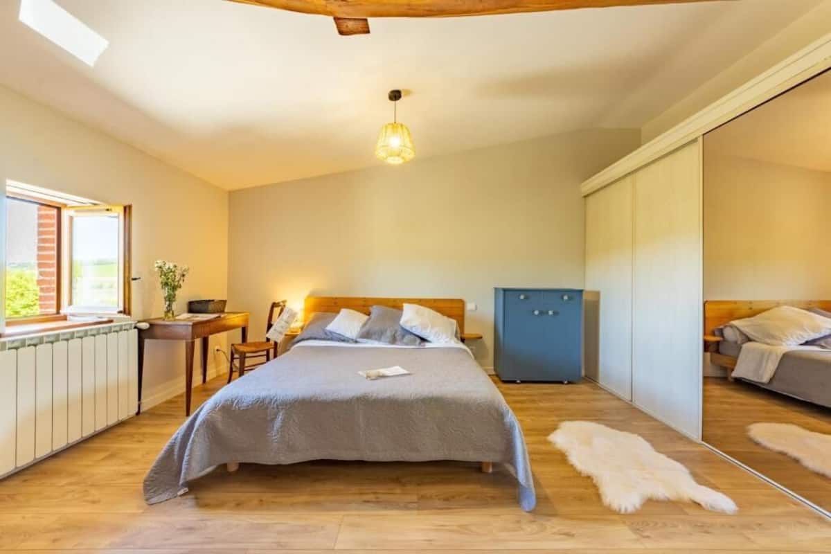 A bedroom with a bed, a desk, a chair, a radiator, a wardrobe, and a mirror.