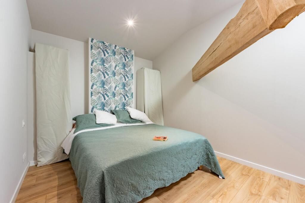 Een slaapkamer met een bed, een hoofdbord met een patroon, een houten balk en een boek op het bed.