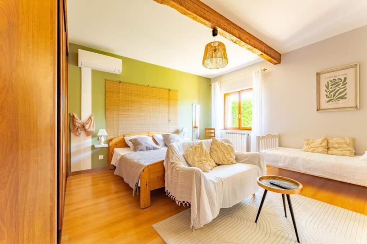 A room with a bed, a sofa, a small table, and a hanging light fixture.