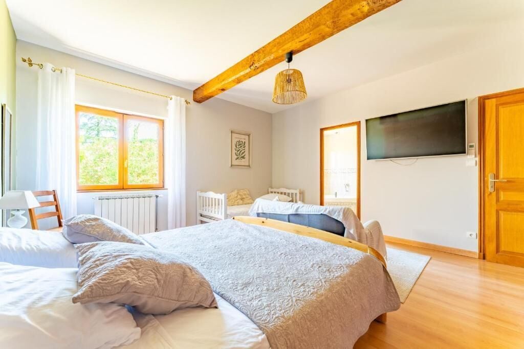 Een slaapkamer met een groot bed, een houten balk in het plafond, een televisie en een raam met gordijnen.