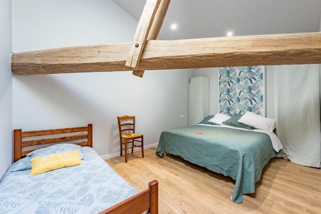 Un dormitorio con techo inclinado, una cama con colcha estampada, una silla y una ventana con cortinas.
