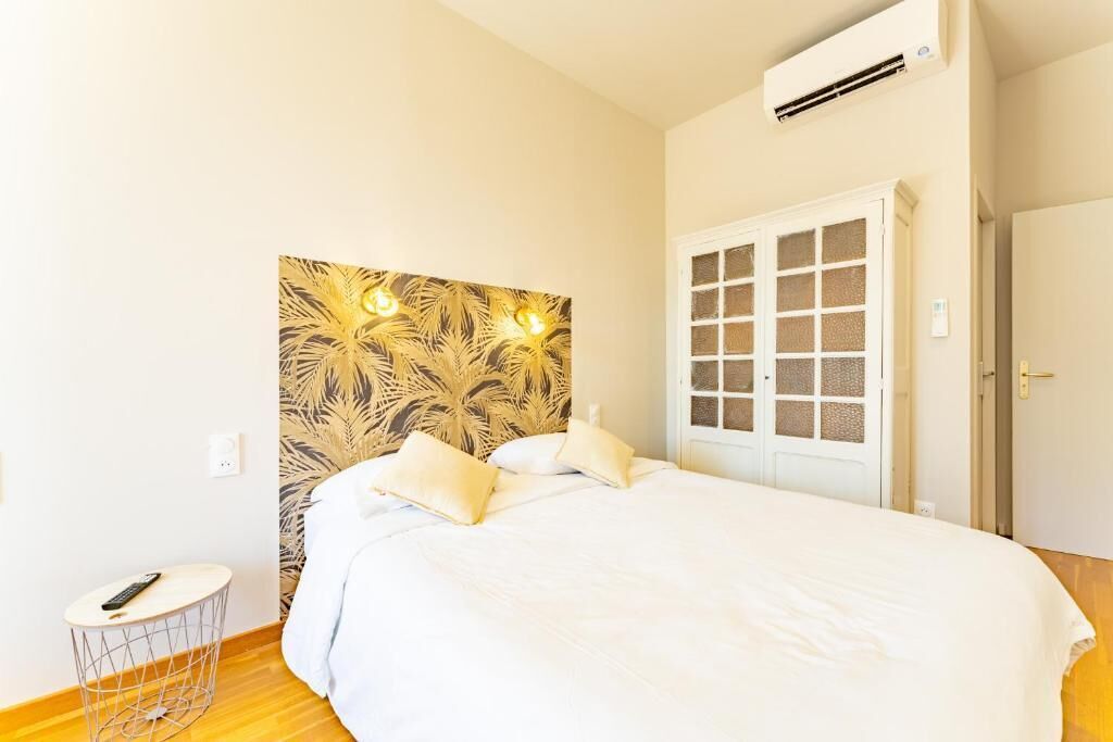 A room with a bed, a small round table, an air conditioning unit, and a door with glass panels.