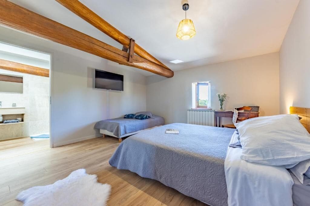 A bedroom with a bed, a desk, a chair, a television, and a window.