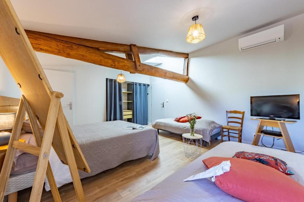 Een slaapkamer met twee bedden, een televisie, een klein tafeltje met een vaas en een houten balk in het plafond.