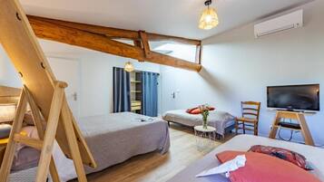 Een slaapkamer met twee bedden, een televisie, een klein tafeltje met een vaas en een houten balk in het plafond.