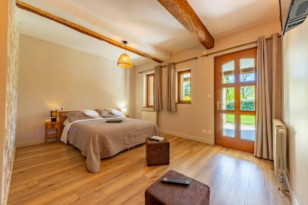 A bedroom with a bed, a nightstand, a reading lamp, a window with curtains, and a wooden floor.