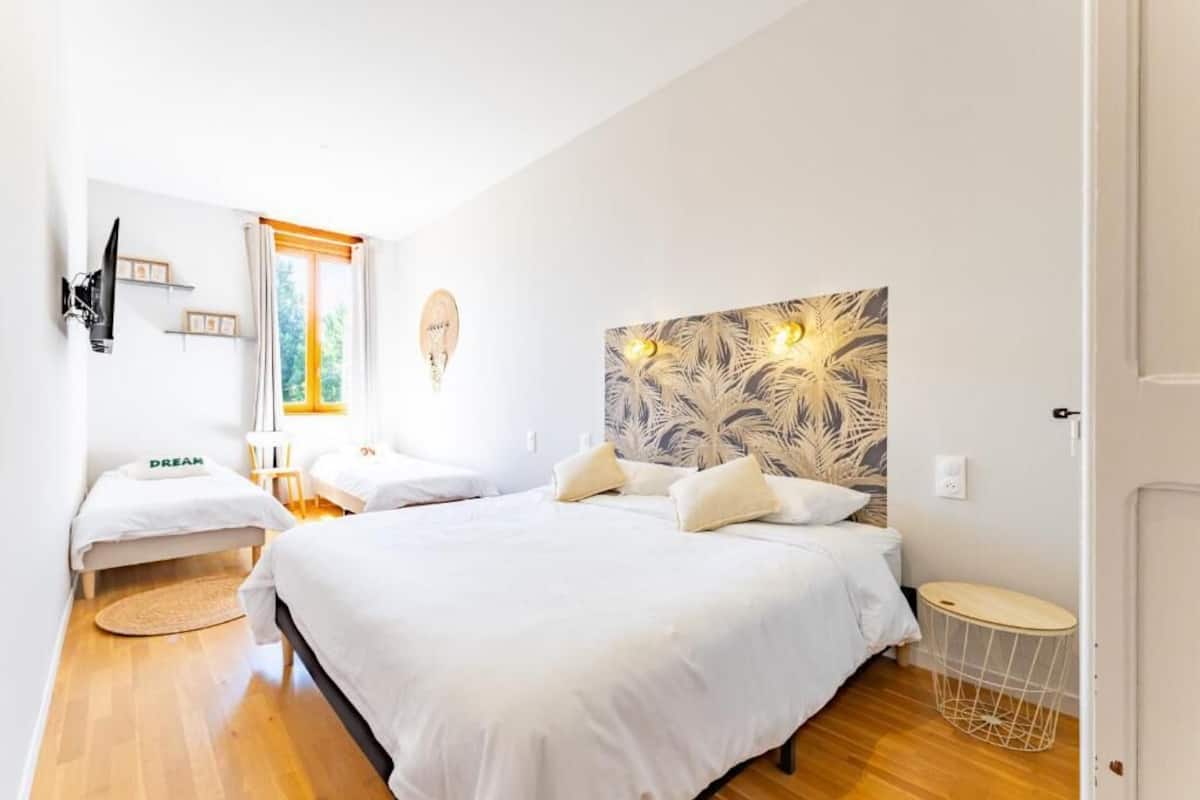 A bedroom with two beds, a large window, a wall-mounted TV, and a decorative headboard.