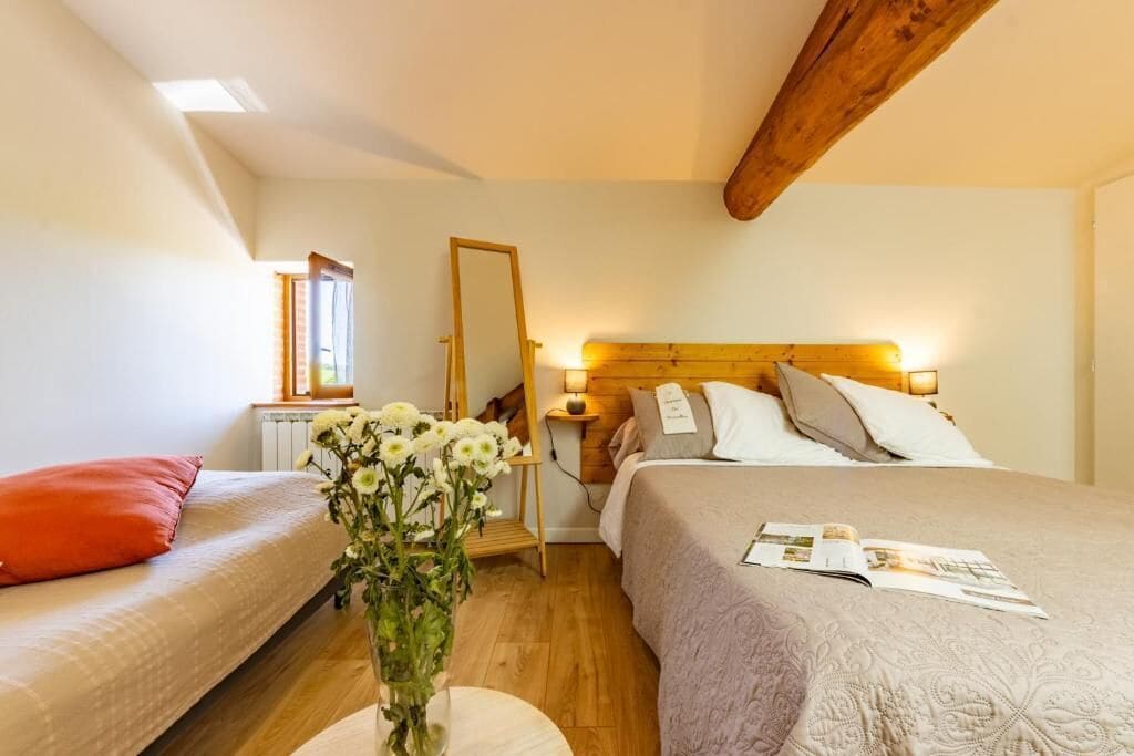 A bedroom with a bed, a bedside table, a mirror, and a window.