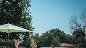 Una piscina con sillas de descanso y un área techada, rodeada de vegetación y edificios.