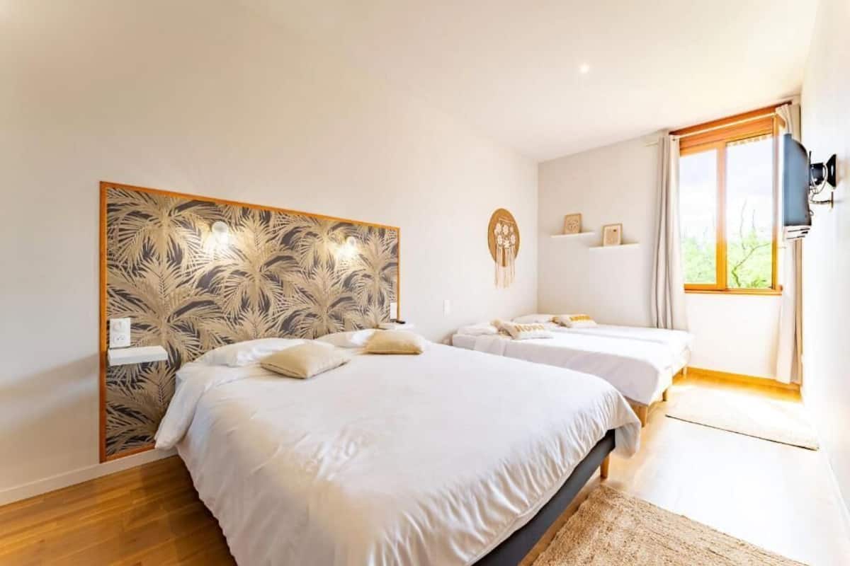 A bedroom with two beds, a decorative headboard, a wall-mounted TV, and a window with curtains.