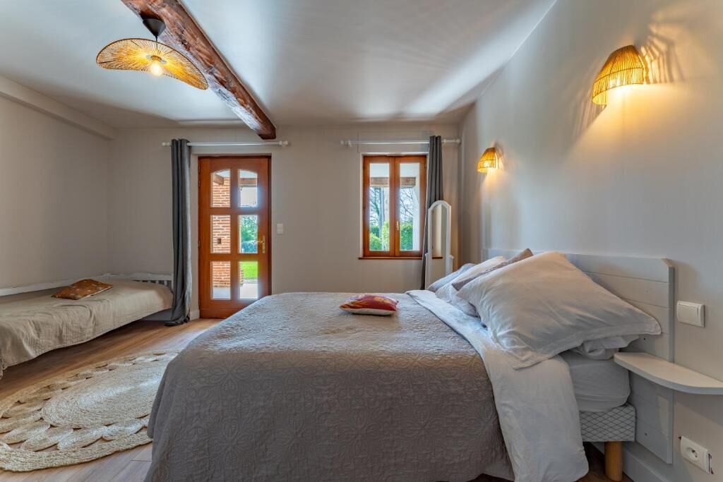 Un dormitorio con cama, mesitas de noche, una ventana y una puerta.
