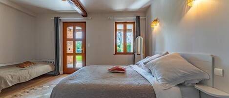 Un dormitorio con cama, mesitas de noche, una ventana y una puerta.