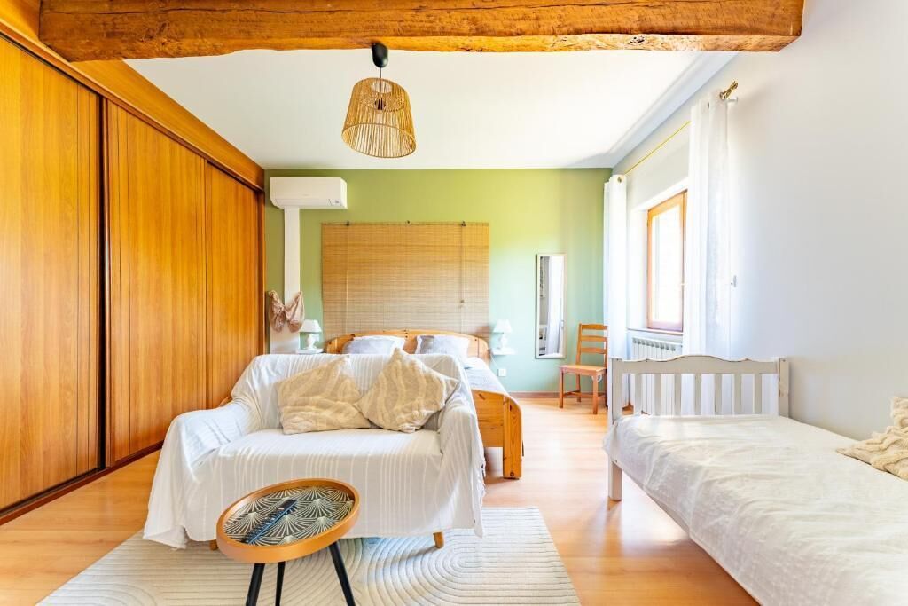 Un dormitorio con cama, mesitas de noche, una silla, una ventana con cortinas y una viga de techo de madera.