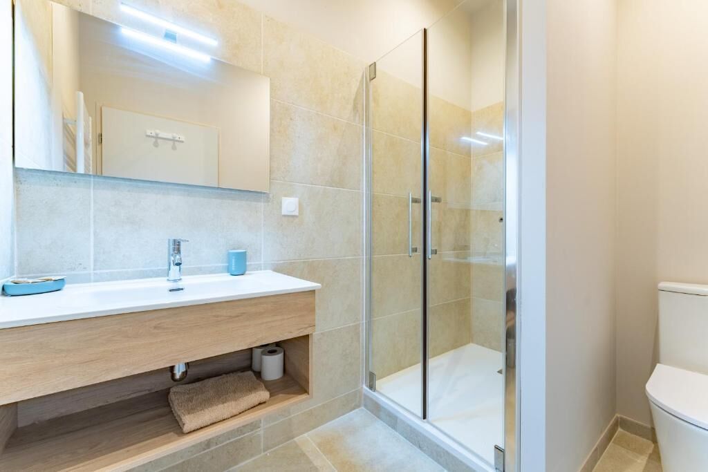 A modern bathroom with a glass shower enclosure, a wooden vanity, and a white toilet.