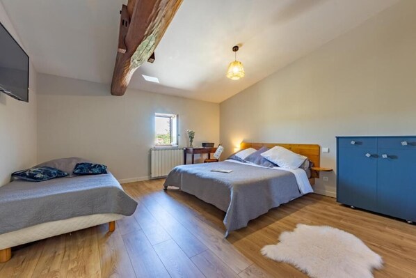 A bedroom with two beds, a wooden ceiling beam, a radiator, a window, and a blue wardrobe. - Ô DOMAINE (Saint-Nauphary)