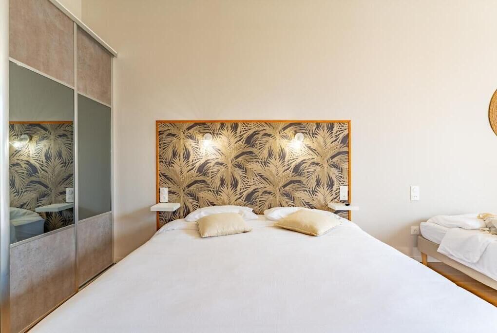 Un dormitorio con una cama grande, cabecera con diseño de hojas, mesitas de noche y un espejo.