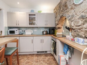 A kitchen with white cabinets, a microwave, a stove, and a stone wall. - Charming Dolfor Retreat in Nefyn (Pwllheli)