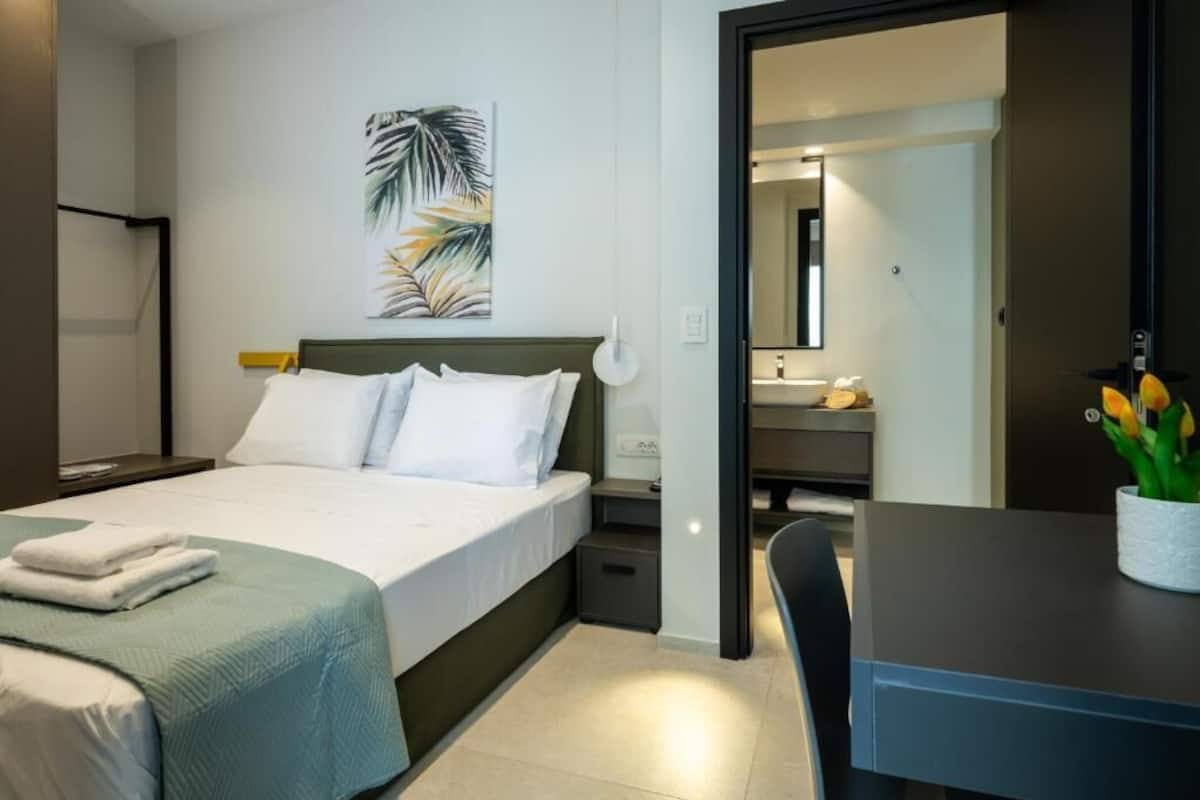 A modern hotel room with a bed, bedside table, and a desk with a chair.