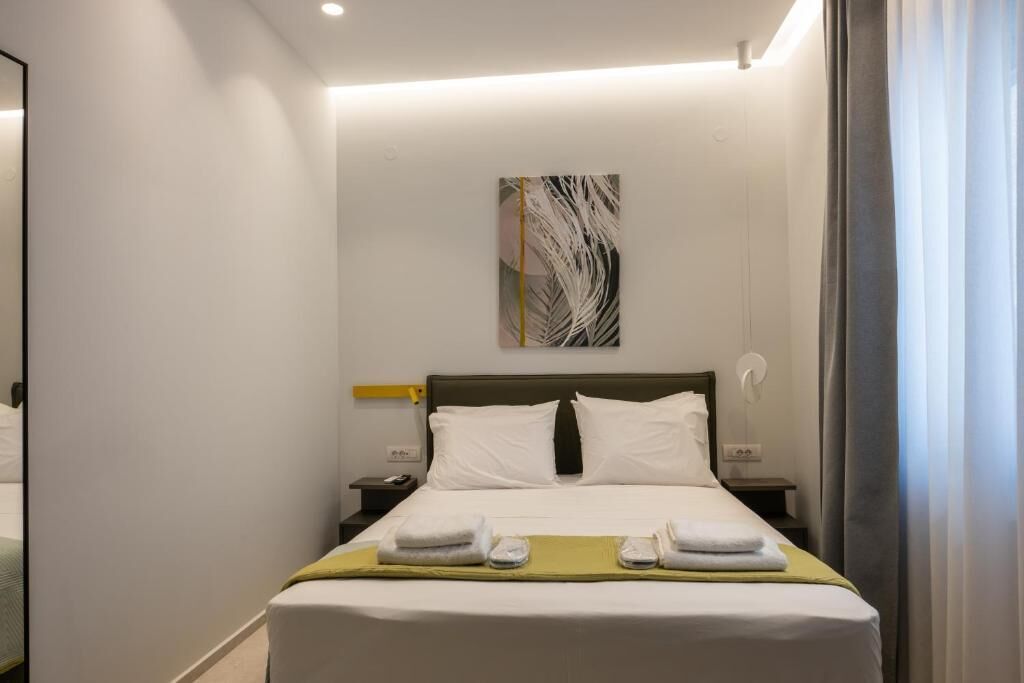 A hotel room with a bed, a bedside table, a nightstand, a wall-mounted artwork, and a window with curtains.