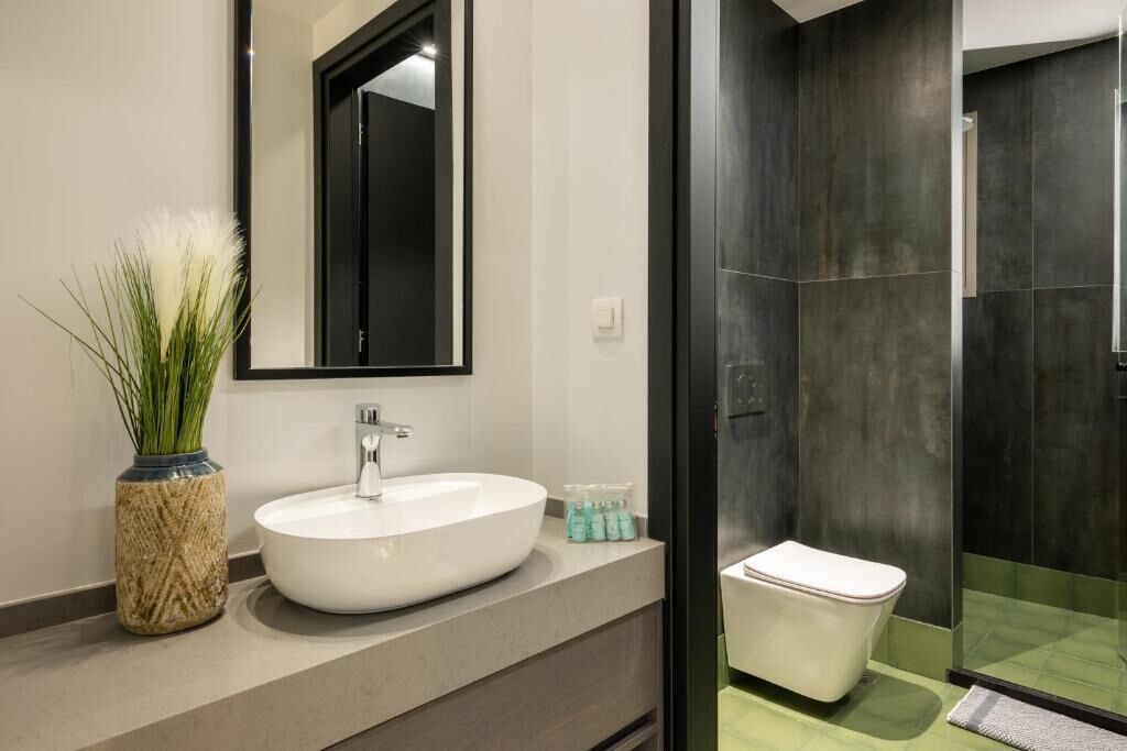 Un baño moderno con lavamanos blanco, un espejo grande, inodoro y cabina de ducha de vidrio.