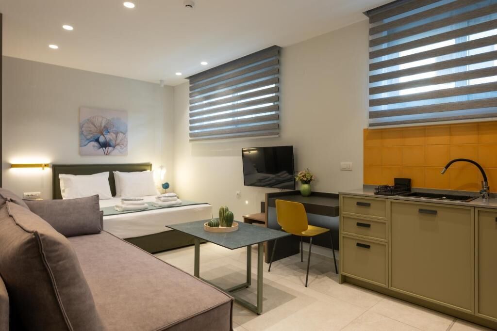 Ein modernes Hotelzimmer mit Bett, Nachttisch, Fernseher, Küchenzeile und Essbereich.
