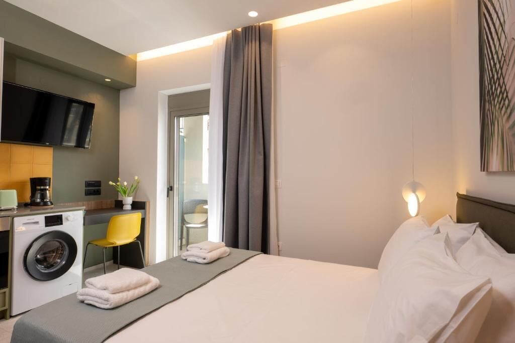 Une chambre d’hôtel équipée d’un lit, d’un bureau avec une machine à laver, d’une chaise et d’un téléviseur fixé au mur.
