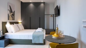 Ein modernes Hotelzimmer mit Bett, Nachttisch, Fernseher und einem Essbereich mit Tisch und Stühlen.