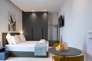 Una habitación de hotel moderna con cama, mesita de noche, televisor y una zona de comedor con mesa y sillas.