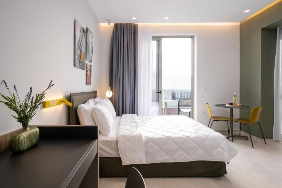 Une chambre d’hôtel comprenant un lit, un bureau, une chaise, une petite table, une plante et un balcon avec une table et des chaises.