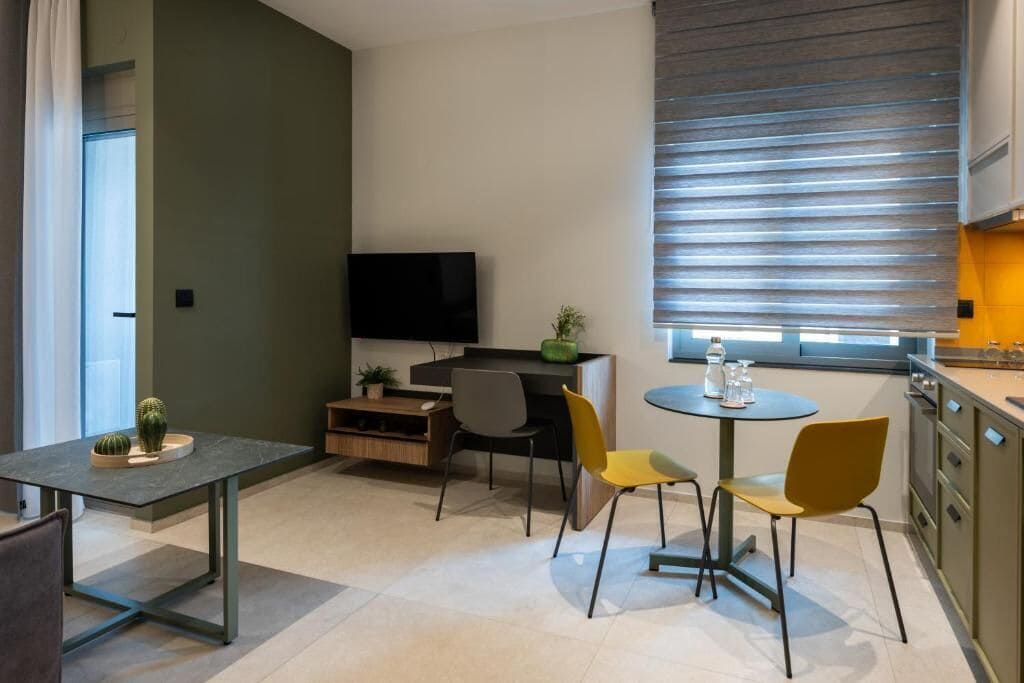 Um espaço de estar compacto com área de jantar, TV, cozinha e janela com persianas.