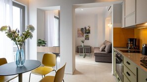 Eine moderne Küche mit Kaffeemaschine, ein Essbereich mit rundem Tisch und gelben Stühlen sowie eine Wohnbereich mit Sofa und Couchtisch.