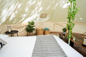 A tent with a bed, a small table, and potted plants.