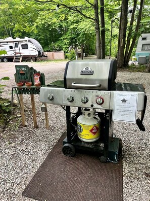 A portable grill with a propane tank, a barbecue sign, and a nearby RV.