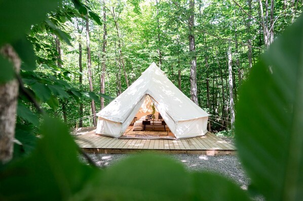 A tented accommodation in a forest with a wooden deck and a view of the surrounding trees.