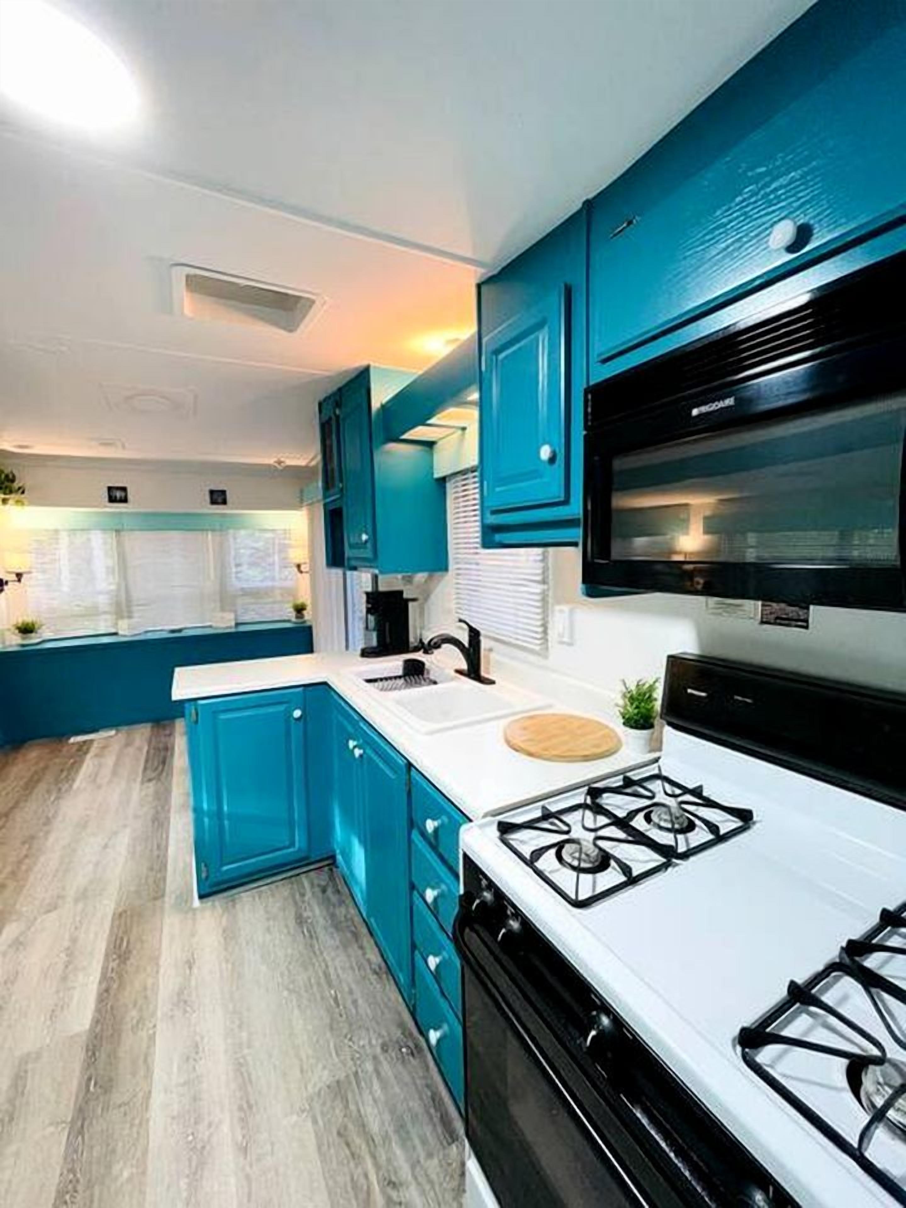 Una cocina moderna con armarios verde azulado, encimera blanca y estufa a gas.