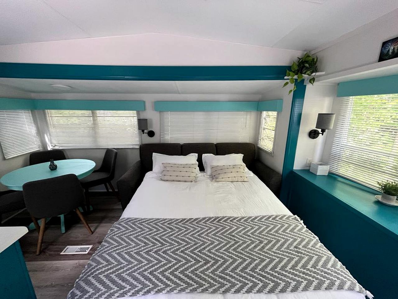 Una habitación con cama, una mesa, sillas y una ventana con persianas.