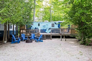 A recreational area with a covered deck, blue Adirondack chairs, and a gravel ground. - Gorgeous and Unique Glamping Caravan near Miller Lake, Perfect for a Weekend of Swimming and Hiking (Miller Lake)
