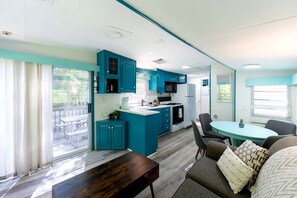 Une cuisine moderne avec des meubles de couleur turquoise, un coin repas doté d’une table ronde et un canapé agrémenté de coussins à motifs.