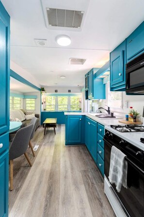 A compact kitchen with teal cabinetry, a dining area with a table and chairs, and a view through the window. - Gorgeous and Unique Glamping Caravan near Miller Lake, Perfect for a Weekend of Swimming and Hiking (Miller Lake)