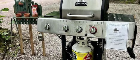 Ein tragbarer Grill mit Propangasflasche, ein Grillplatzschild und ein Wohnmobil in der Nähe.