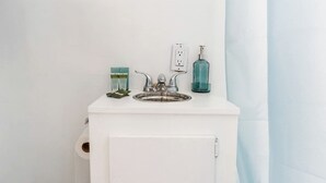 A bathroom with a white sink, a faucet, a soap dispenser, and a glass container.