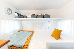A compact room with a bed, a small table, a clock, and a window. - Fully Equipped Glamping Caravan near Miller Lake, Perfect for a Weekend Getaway from Toronto (Miller Lake)