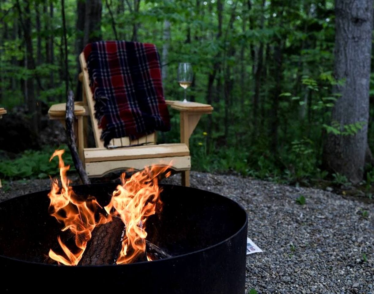 Un feu de camp, une chaise et un verre de vin, le tout dans un cadre forestier.